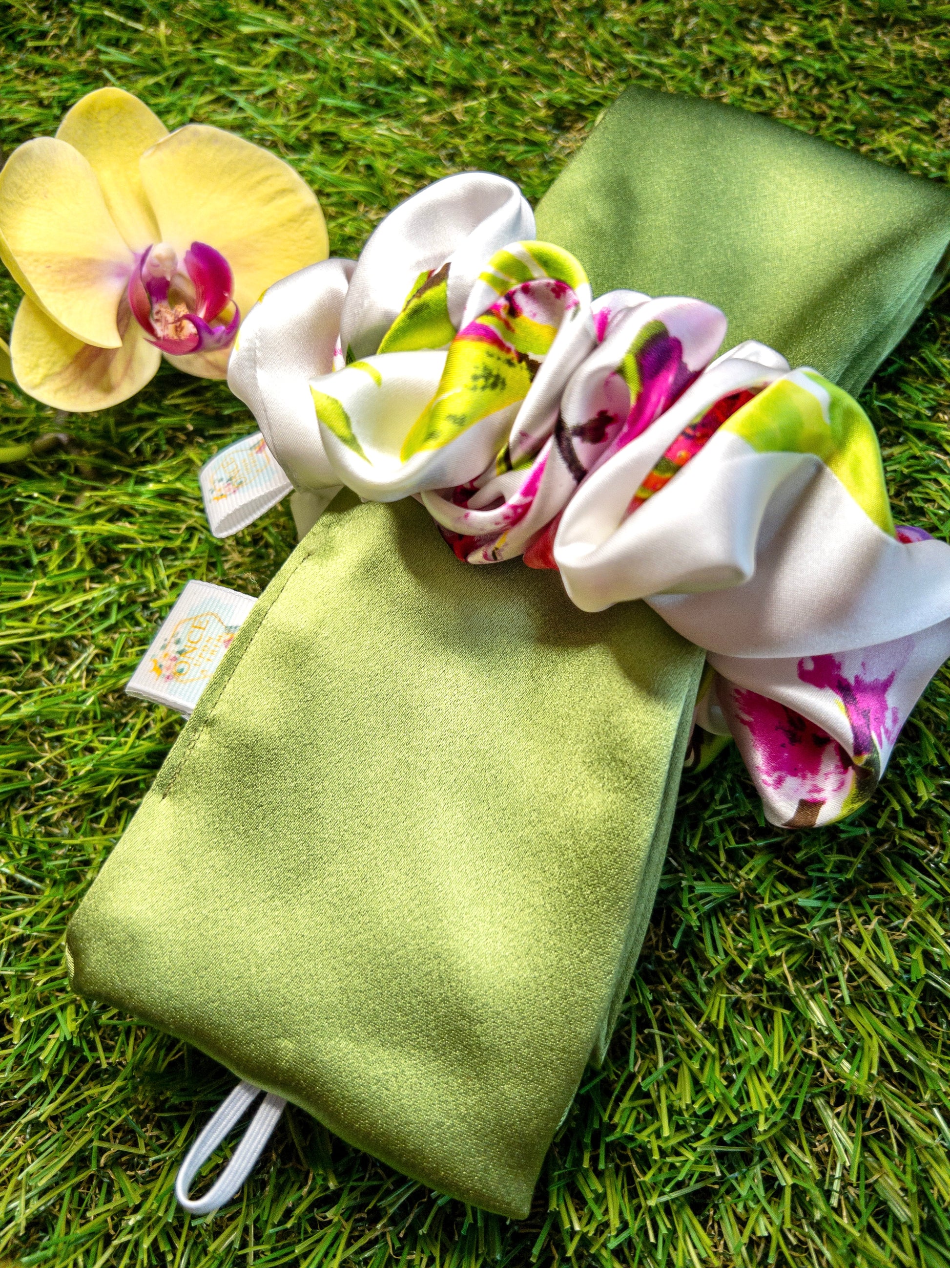 Heatless Curl Silk Hair Tie- Fern & Flora. Green silk tie with white, green & pink floral scrunchie laying on grass.