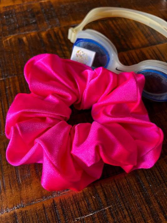 Neon Pink scrunchie laying on wood table with swim goggles. Scrunchie is made of lycra/spandex for gym & beach